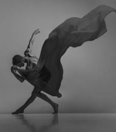 Dancer in an emotional pose with a shadow-like scarf dramatically flowing from his hand into the air with the momentum of his dance